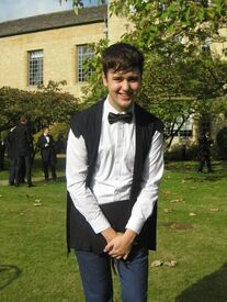 Alfie, who is wearing academic dress and has short dark hair, smiles into the camera