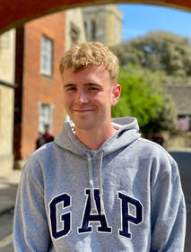 Jack, who has short blonde hair and is wearing a grey hoodie, smiles into the camera. His hoodie reads GAP