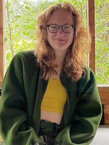 Mia, who has long red hair and is wearing a green cardigan, smiles into the camera