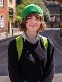 Ruskin, who has medium hair and is wearing a green beanie, smiles into the camera